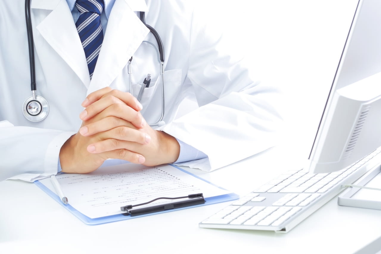 医者が机の上で自分の手を握っている画像